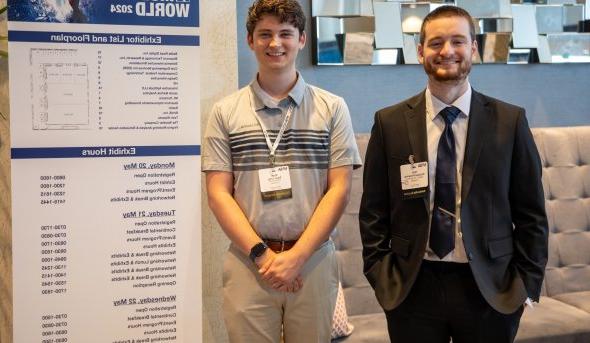 Two young men stand in front of a conference sign.